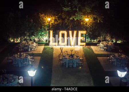 Des tables préparées pour le banquet d'un mariage dans un jardin avec un géant lumineux lettres Banque D'Images