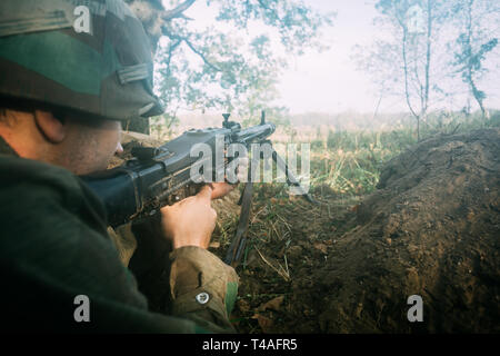 La reconstitution médiévale caché déguisé en soldat d'infanterie de la Wehrmacht allemande dans la seconde guerre mondiale, visant une mitrailleuse à l'ennemi à partir de la tranchée dans la forêt brumeuse. La seconde guerre mondiale WW2 Wea Banque D'Images