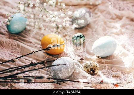 Les oeufs de Pâques élégant avec des fleurs de printemps et des branches de saule sur tissu rustique sous le soleil de la lumière sur le bois. Oeufs colorés moderne peint avec un colorant naturel. Ha Banque D'Images