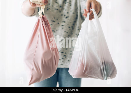 Shopping concept zéro déchet. Femme tenant d'une main d'épicerie réutilisables dans un sac écologique et dans d'autres légumes dans du plastique sac de polyéthylène. Choisissez plast Banque D'Images