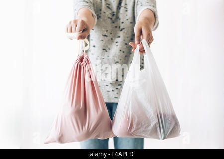 Interdire un usage unique en matière plastique. Shopping concept zéro déchet. Femme tenant d'une main d'épicerie réutilisables dans un sac écologique et dans d'autres légumes en polyet en plastique Banque D'Images