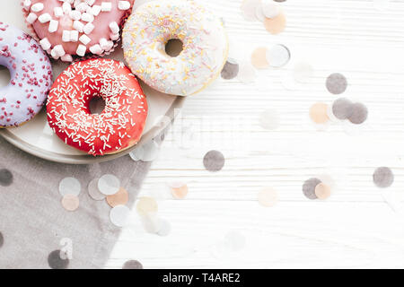 Délicieux donuts colorés avec sprinkles sur plaque sur le tableau blanc élégant avec confetti, télévision lay. Partie concept. Pas de régime alimentaire. Candy bar at wedding recepti Banque D'Images