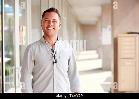 Portrait Of Smiling Male School Teacher Standing In Corridor of College Building Banque D'Images