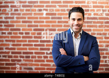 Portrait Of Smiling businessman standing Against brick wall in Modern Office Banque D'Images