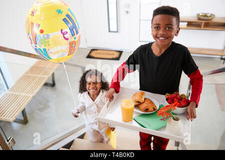 Portrait des enfants portant les parents le petit déjeuner au lit sur plateau avec ballon pour célébrer Anniversaire Banque D'Images