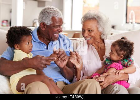 Les grands-parents Sitting on Sofa At Home Jouer avec bébé petites-filles Banque D'Images