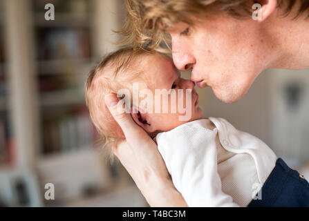 Un jeune père tenant un bébé nouveau-né à la maison, à l'embrasser. Banque D'Images