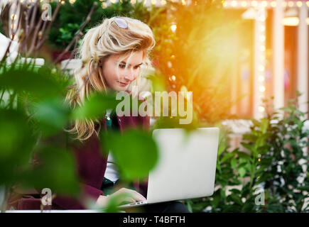 Une belle jeune fille est assise sur un banc avec un ordinateur portable dans ses mains sur une nouvelle rue avec la ville. Un concept de travail plaisir Banque D'Images