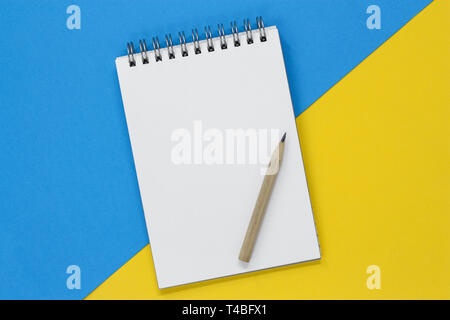 Ouvrez Carnet à spirales avec une page blanche sur un fond bleu et jaune, avec l'exemplaire de l'espace. Banque D'Images