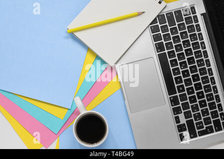 Télévision lay photo d'un espace de travail créatif. Vue de dessus de bureau avec un papier pastel multicolores, le bloc-notes et crayon, ordinateur portable et Coffee cup with copy space. Banque D'Images