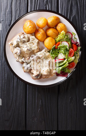 Escalope de porc en sauce crémeuse aux champignons avec une salade de pommes de terre fraîches et de légumes grillés sur une plaque. Haut Vertical Vue de dessus Banque D'Images