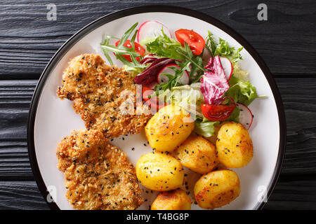 Servir les steaks frites dans de la panure de sésame avec de nouvelles pommes de terre et salade fraîche gros plan sur une assiette sur la table. haut horizontale Vue de dessus Banque D'Images