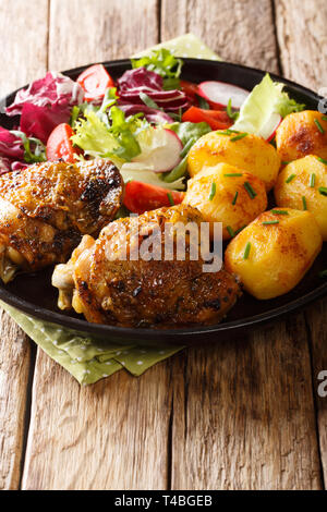 Cuisses de poulet délicieux servi avec de jeunes pommes de terre et salade fraîche gros plan sur une plaque verticale sur la table. Banque D'Images