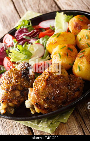 Cuisses de poulet rôti avec pommes de terre et salade fraîche gros plan sur la plaque sur la table verticale. Banque D'Images