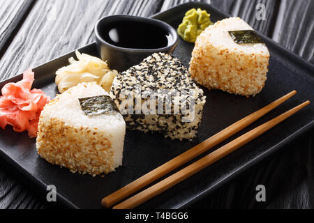 Onigiri sésame en servi avec sauce au gingembre et wasabi, close-up sur une plaque sur la table horizontale. Banque D'Images