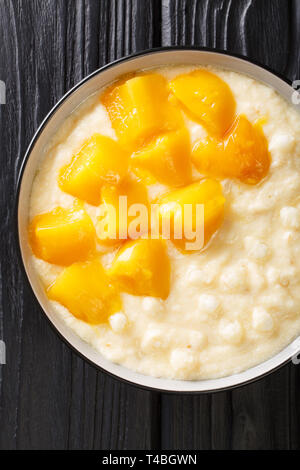 Pouding au tapioca asiatique traditionnel avec du lait de coco et mangue fraîche close-up dans un bol sur la table. Haut Vertical Vue de dessus Banque D'Images