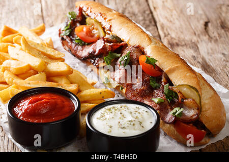 Sandwich fait maison avec du bacon et des légumes servis avec frites et sauces close-up sur la table horizontale. Banque D'Images