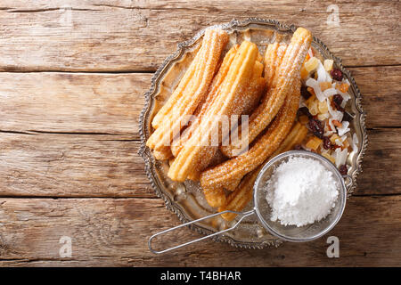 Churros chauds fraîchement préparés avec du sucre en poudre et de fruits confits close-up sur la table supérieure horizontale. Vue de dessus Banque D'Images