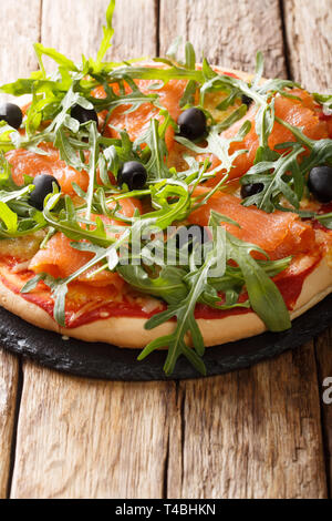 Pizza italienne maison avec du saumon salé, roquette fraîche, olives et fromage libre sur la table verticale. Banque D'Images