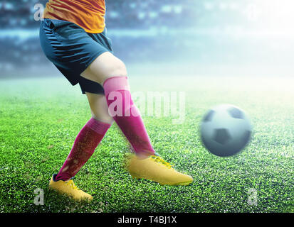 Joueur de football femme en jersey orange Kicking the ball sur le terrain de football Banque D'Images