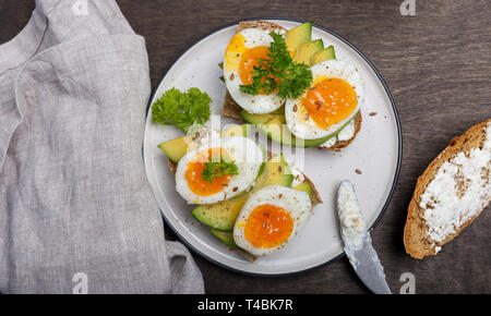 Délicieux toasts au fromage à la crème, d'avocat et oeufs sur plaque blanche avec un couteau et une serviette au fond de bois. Concept de petit-déjeuner avec des oeufs Banque D'Images