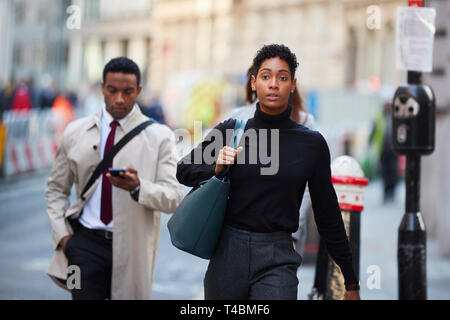 Jeune femme noire marchant dans une rue de Londres exerçant son sac à main, front view Banque D'Images