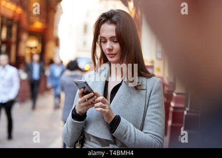 Jeune femme blanche debout sur une longue rue de Londres en utilisant smartphone, Close up, selective focus Banque D'Images