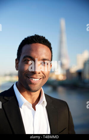Jeune black businessman dans smart casual clothing debout près de la Tamise à Londres smiling to camera, Close up Banque D'Images