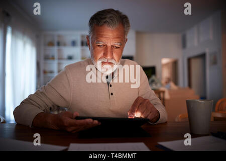 Senior homme assis à une table de lecture d'un e livre à la maison le soir, Close up Banque D'Images