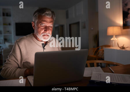 Senior Hispanic man ses finances en direct à la maison en utilisant un ordinateur portable dans la nuit Banque D'Images