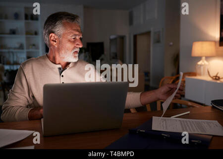 Senior Hispanic man ses finances en direct à la maison en utilisant un ordinateur portable dans la nuit Banque D'Images