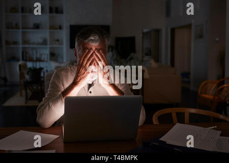 Senior Hispanic man ses finances en direct à la maison en utilisant un ordinateur portable dans la nuit Banque D'Images