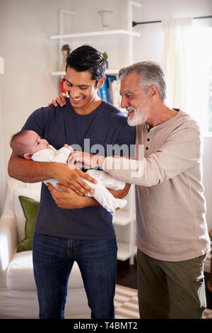 Fier senior Hispanic man standing avec son fils adulte en tenant son petit garçon de quatre mois, vertical Banque D'Images