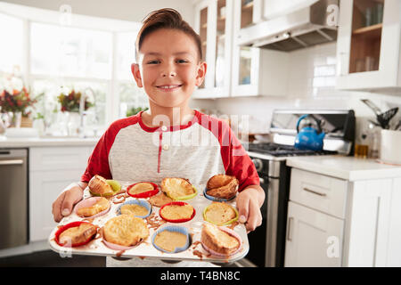 Fier pre-teen boy standing in kitchen présentant les gâteaux qu'il a fait à l'appareil photo, Close up Banque D'Images