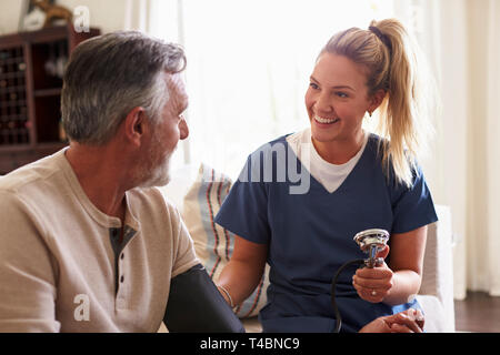 Travailleur de la santé des femmes accueil faire visite à un homme de prendre sa pression artérielle, Close up Banque D'Images
