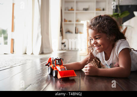 Jeune fille hispanique allongée par terre dans le salon à jouer avec un jouet Camion excavateur Banque D'Images