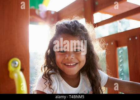 Young Hispanic girl playing sur une escalade dans une aire smiling to camera, rétroéclairé, Close up Banque D'Images