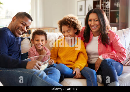 Séance jeune grands-parents avec leurs petits-enfants sur le canapé dans le salon eating popcorn et riant, vue de face, Close up Banque D'Images