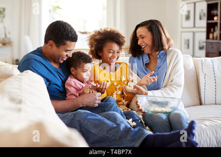 Young mixed race family assis ensemble sur le canapé dans son salon à regarder un film d'horreur, de compensation les dépôts de pop-corn, selective focus Banque D'Images