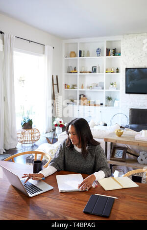 Portrait of middle aged woman sitting at the table dans sa salle à manger à l'aide d'un ordinateur portable, vertical Banque D'Images