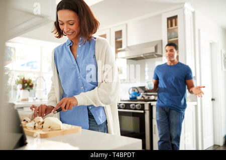 Young mixed race woman standing dans la cuisine la préparation des aliments, son partenaire debout derrière parler, l'accent sur le premier plan Banque D'Images