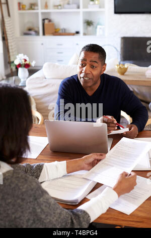 L'homme millénaire avec un ordinateur portable en donnant des conseils financiers à une femme assise à la table détient un document dans sa salle à manger, elevated view, vertical Banque D'Images