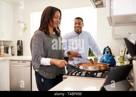 Middle aged hispanic couple dans la cuisine la préparation des aliments sur la plaque de cuisson à l'aide d'une fiche sur un ordinateur tablette, selective focus Banque D'Images