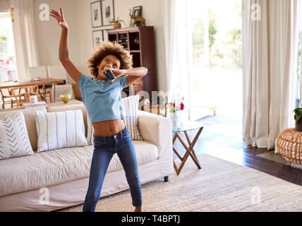 Pré-ado fille danser et chanter le long de la musique dans la salle de séjour à la maison en utilisant son téléphone comme un microphone, Banque D'Images