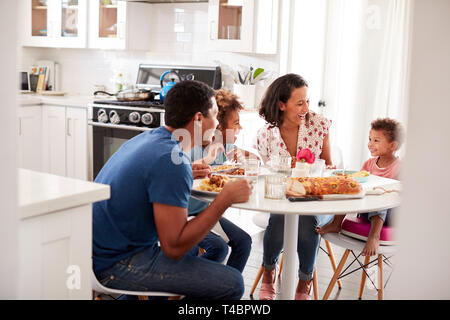 Young mixed race famille manger un repas ensemble à la table de leur cuisine, vu de porte Banque D'Images