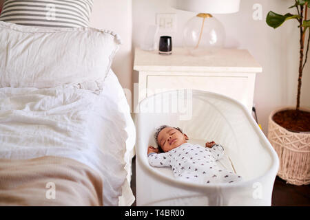 Trois mois bébé endormi dans son lit à côté du lit dans la chambre de sa mère Banque D'Images