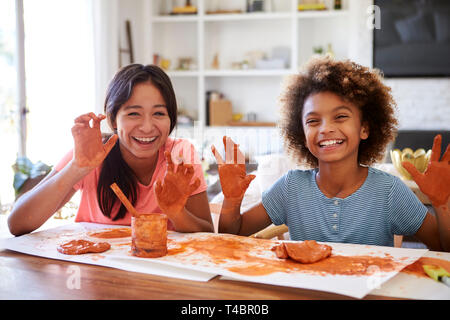 Deux copines s'amusant à jouer avec de la pâte à modeler à la maison, souriant et montrant les mains sales à l'appareil photo, vue de face, Close up Banque D'Images