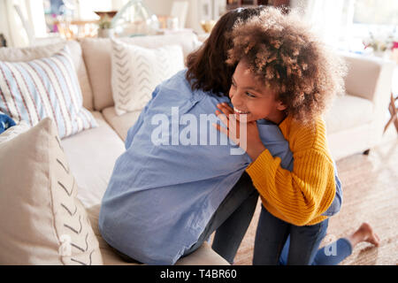 Pre-teen girl hugging her mother sitting on sofa dans le salon, d'élevé, vue arrière