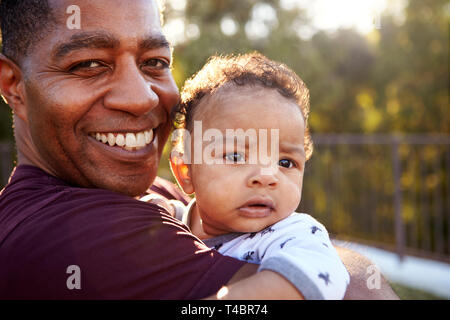 Fier grand-père millénaire comité permanent dans le jardin, tenant son petit-fils âgé de trois mois et souriant à la caméra, Close up, tête et épaules Banque D'Images