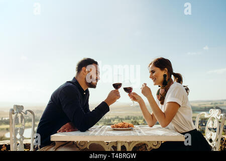 Smiling couple assis dans un restaurant toasting verre de vin rouge. Couple heureux sur une date de parler les uns aux autres holding verre de vin. Banque D'Images